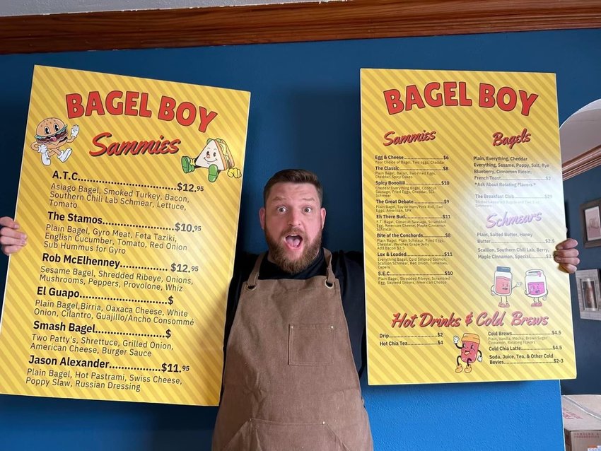 Alex Warner poses with the new menu for Bagel Boy, which is set to expand to dine-in services after offering drive-through and pop-up bagel sandwiches and coffee since the summer of 2022.