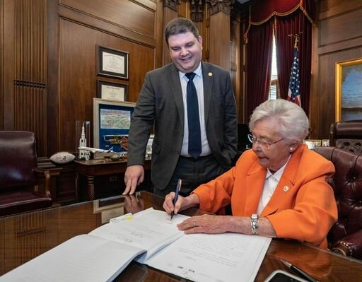 Rep. Matt Simpson watches at Gov. Kay Ivey signs HB1 into law.