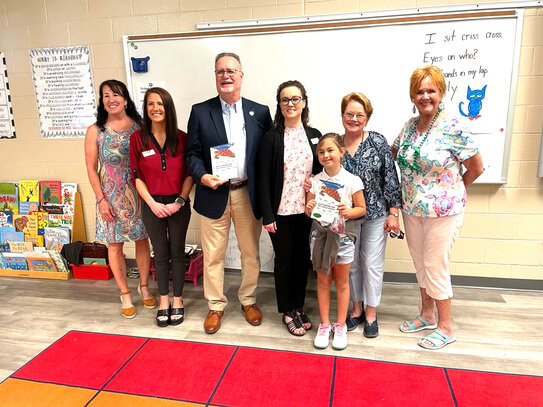 Linda B. Schmitz Spangrud poses with members of Foley Elementary School and her book &ldquo;Miss Sandra and the Turtle People.&rdquo; To the right, a scene from Newton Elementary School.