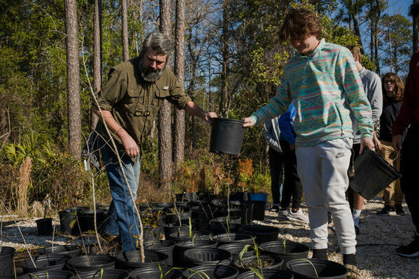 Gulf Shores High School Horticulture and Environmental Management teacher Will Tuggle hands off small potted trees to students that will be planted.