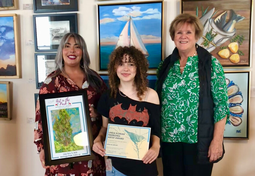Foley Art Center Executive Director Chloe Salina and Art in the Park Committee member Darrelyn Dunmore present Laila Al-Biyati with the Linda Koniar Emerging Artist of the Year award, along with a framed festival poster and a set of art supplies.