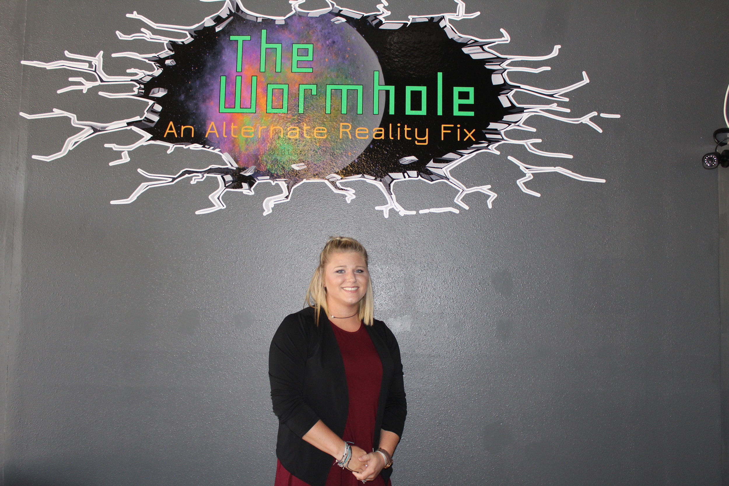 Lauren Lowery, co-owner of The Wormhole, under the logo of her design. Lauren and her husband, Shane, have brought Baldwin County a fun and exciting gaming opportunity.