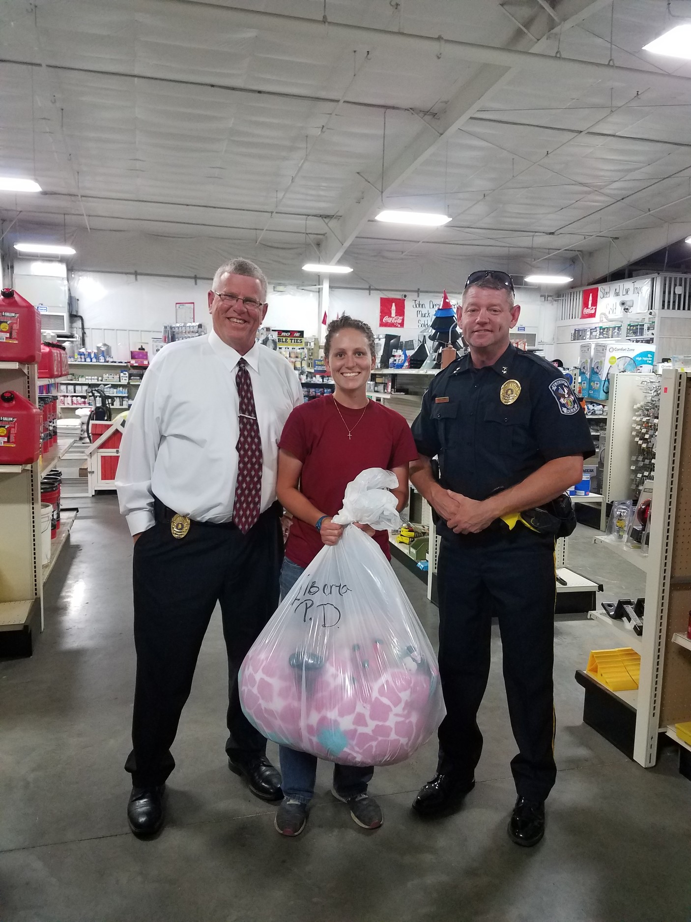 Elberta Police Chief Cliff Roberts, Elberta Farmers Co-Op employee Kristen Edwards, and Elberta Assistant Chief of Police Ryan Pelfrey, along with the bag of donated stuffed animals that was given to the police department.