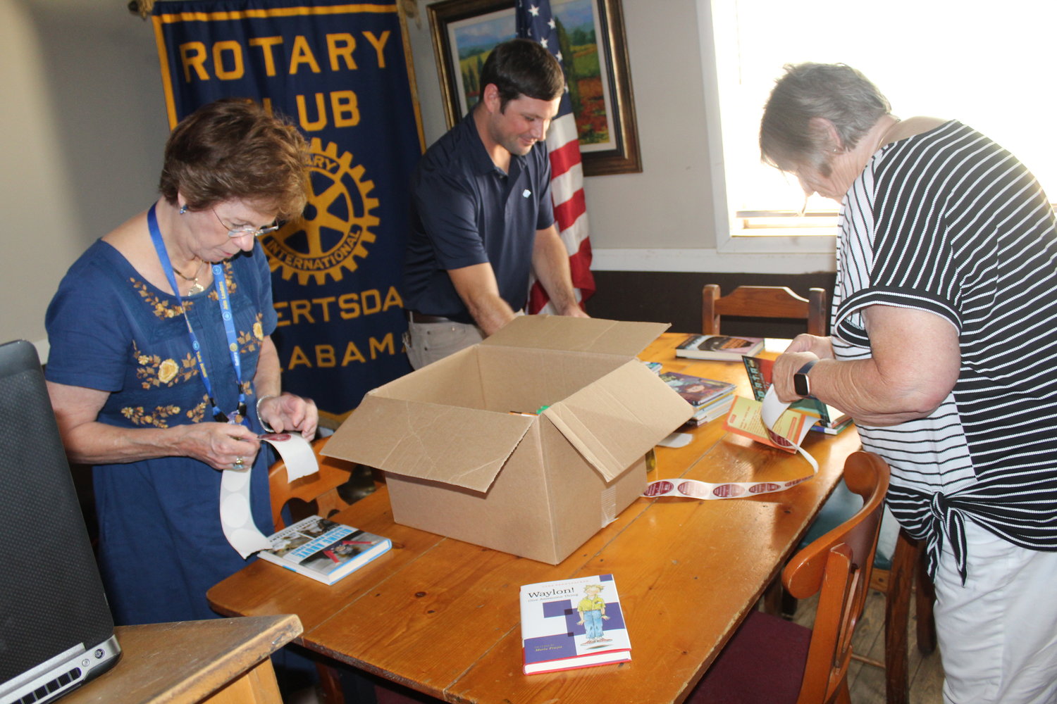Members of the Robertsdale Rotary Club place stickers in books to donate to Elsanor School’s “Little Library That Could.”