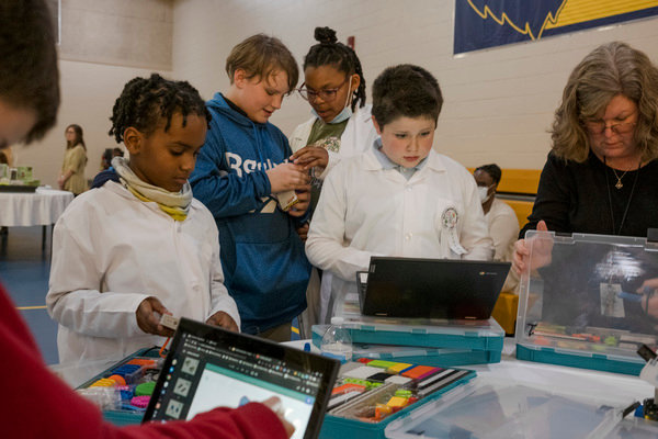 Students, some in lab coats, program robots in the gym during Foley Elementary's first STEAM night.