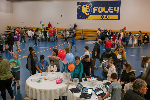 Students and their families move around to different tables in the gym at Foley Elementary during the school's first STEAM night.