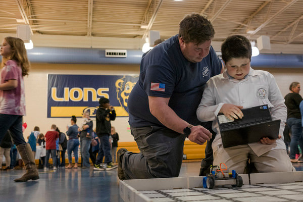 Jackson Bagby, a 3rd grader at Foley Elementary, shows his dad, Terran Bagby, how to control the robot he programmed at the school's first STEAM night.