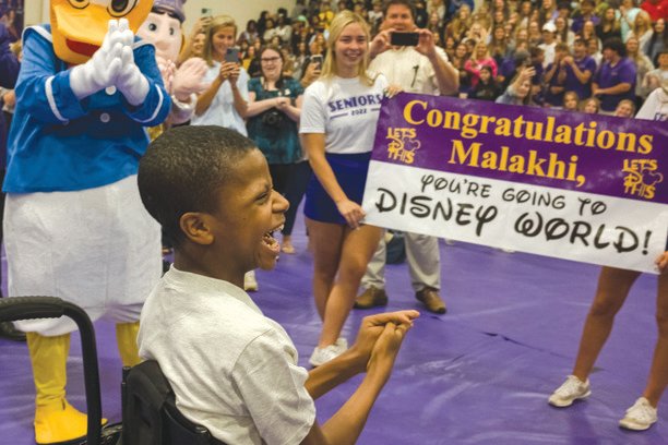Malakhi Washington smiles as Donald Duck and others looks on at Daphne High School on Friday after Washington was surprised with a free trip to Disney World through Magic Moments, an Alabama-based company that provides children diagnosed with chronic, life-threatening illnesses with opportunities to live out their dreams.