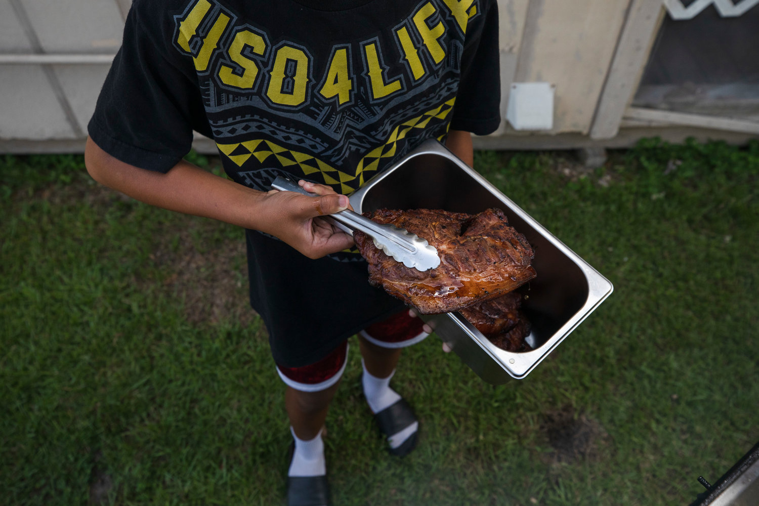 Niu Faiupu’s son Abraham retrieves Aloha Made BBQ pork from the smoker before taking it to the food truck in Fairhope on Nicholas Avenue Tuesday afternoon.