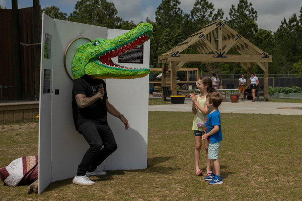 JD Swiger, with Swiger Studios, shows two small patrons how to use ‘Chuckie’, an interactive art display that was modeled after Gulf Coast Zoo’s 12ft American alligator. Swiger made the piece with hundreds of plastic beach toys recovered and donated by zookeepers and unveiled the piece at the zoo’s Earth Day celebration.