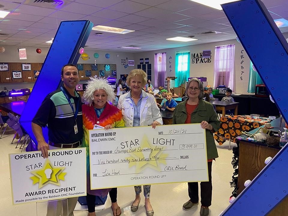 Baldwin EMC Charitable Foundation Board Members Mary Lou McMillan (second from right) and Bonnie Schell (far right) present a Star Light award to Lisa Hood (second from left), accompanied by Assistant Principal Spencer Segrest (left), at Fairhope East Elementary School for the 2021-2022 school year.