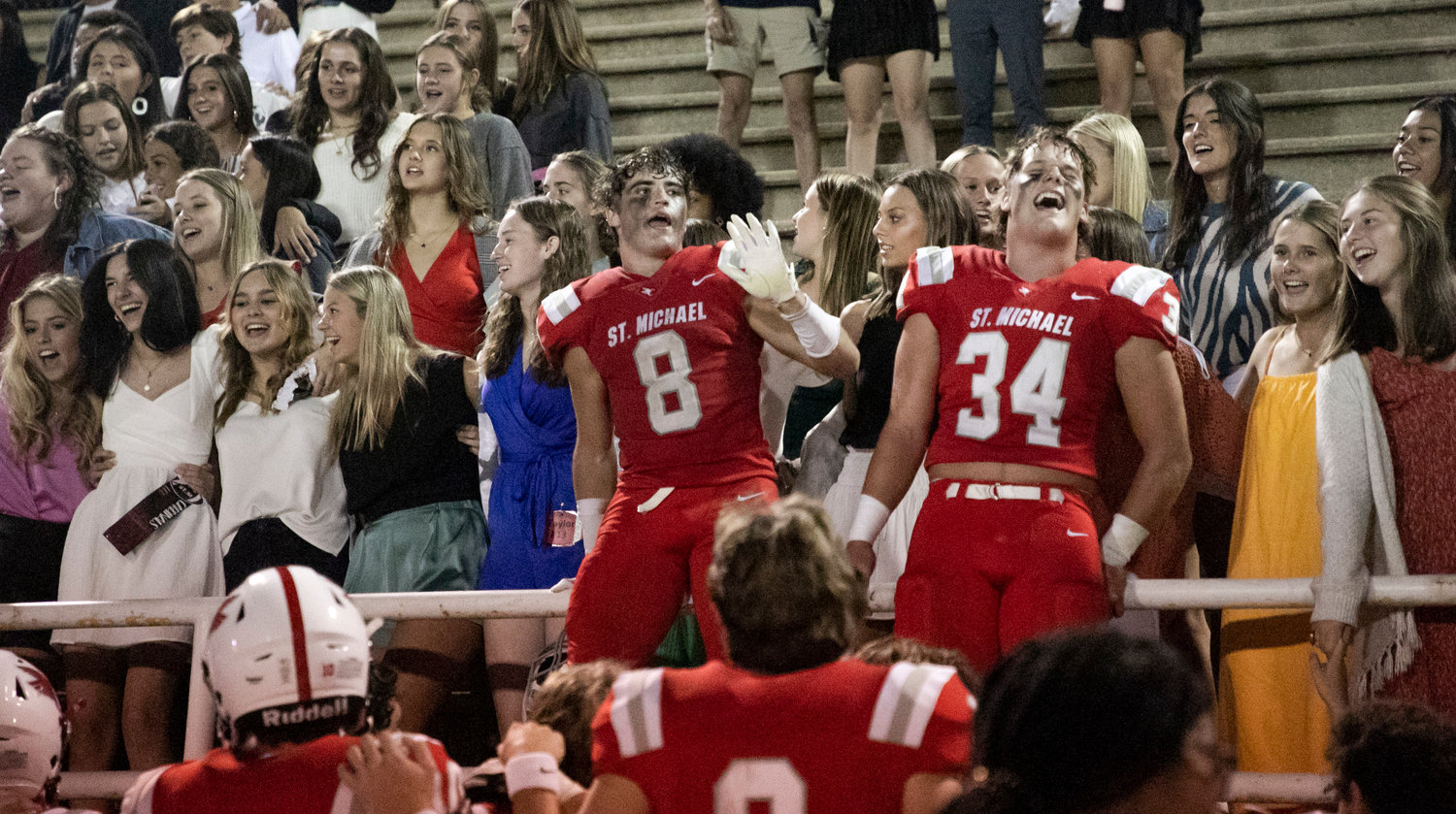 Cardinal seniors Ezra Sexton (8) and Tyler Cella (34) joined the student section to sing St. Michael Catholic’s alma mater after they beat Orange Beach, 49-41, Thursday night on W. C. Majors Field at Fairhope Municipal Stadium.