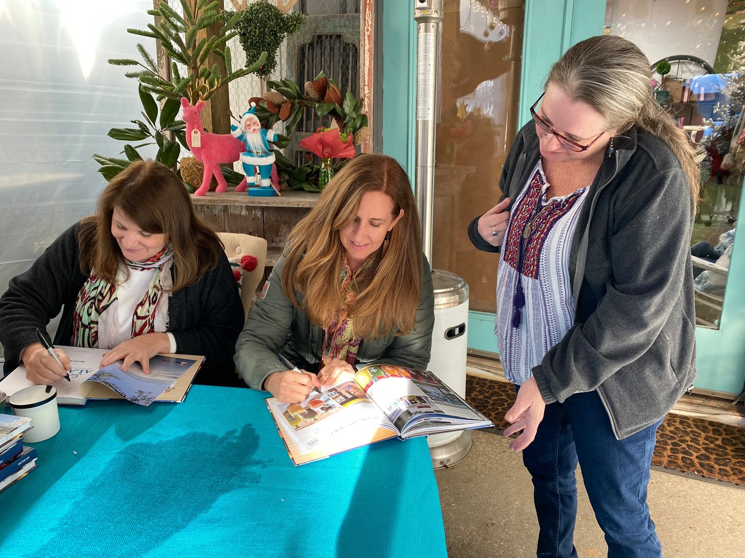 (From left) Martie Duncan signed books at The Garage Studio in Fairhope just before Christmas. Lorie Ward, owner of Fairhope Juice Company signed the page she is featured on for Maegan Bratton, owner of Cowbell Rolled Ice Cream in Gulf Shores.
