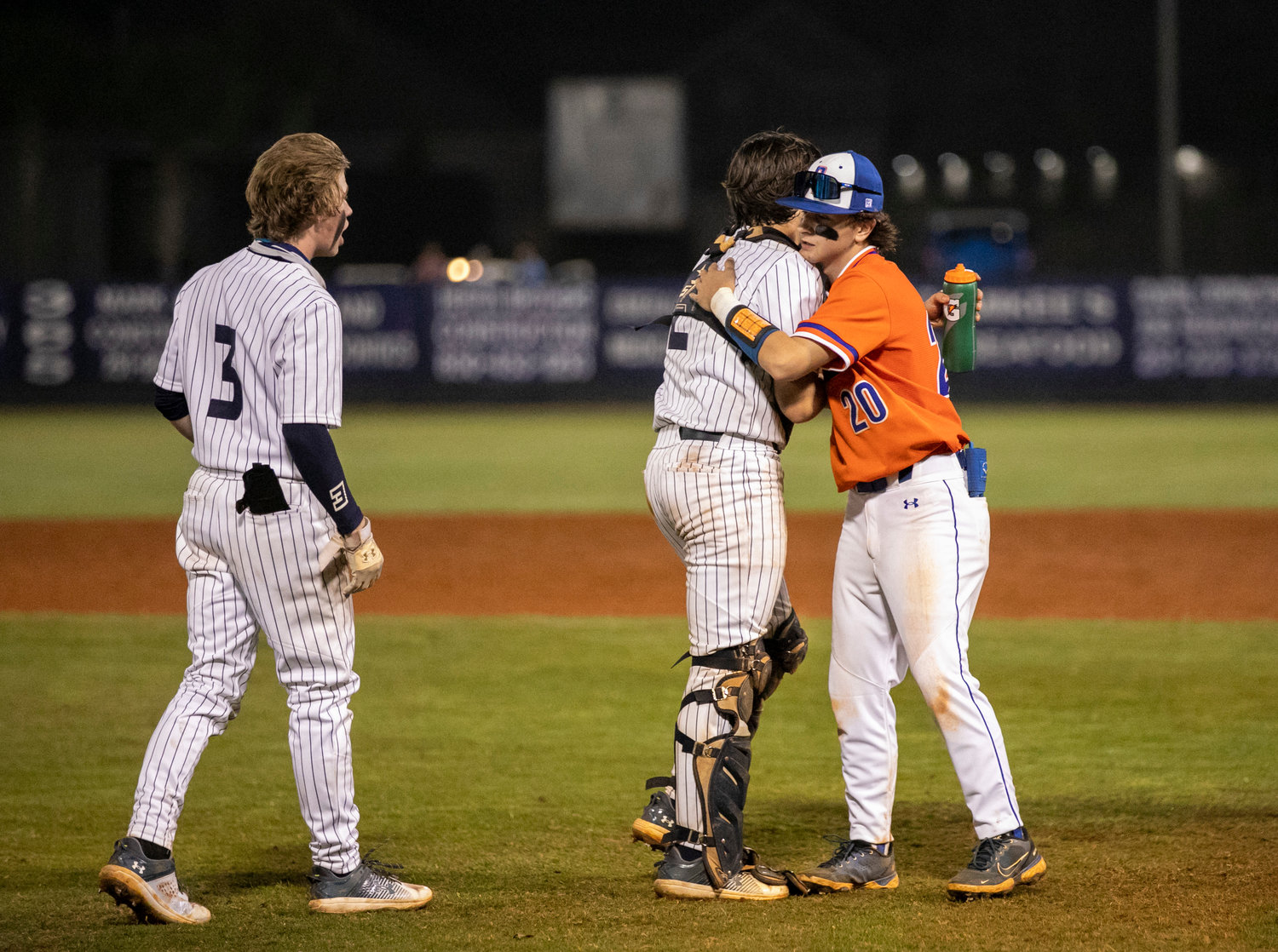 Gulf Shores’ Dom Maldet (2) and Orange Beach’s Tucker West (20) share an embrace after the first-ever baseball game between the Dolphins and Makos at the Gulf Shores Sportsplex Friday night, Feb. 24, as part of Prep Baseball Report’s South Alabama Showdown. The host Dolphins won 10-0.