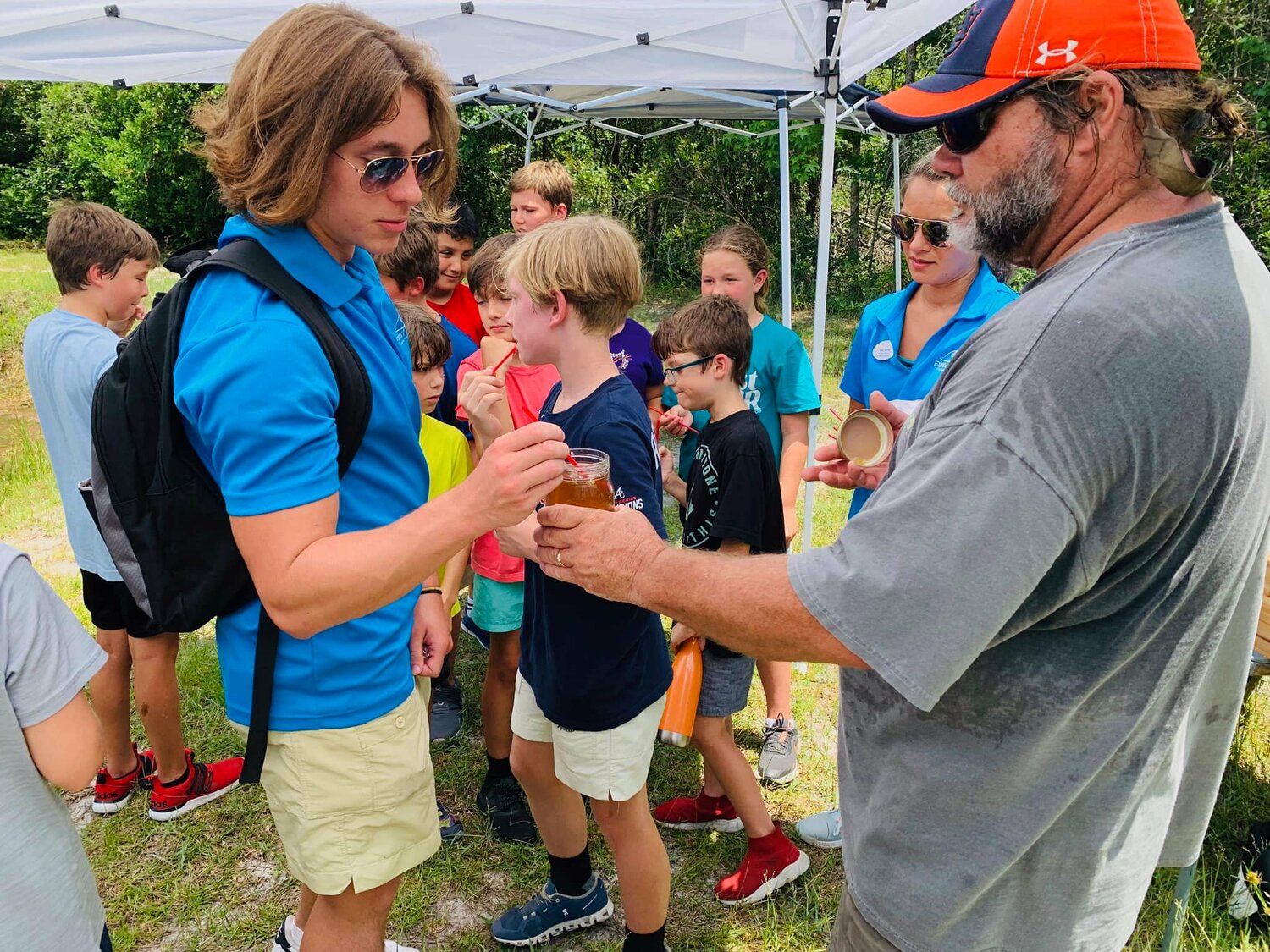 Christ Litton (right) offers an Expect Excellence counselor a sample of honey during an Expect Excellence summer camp field trip. Litton show the children his bee hives located at Island Church and taught them about the process.