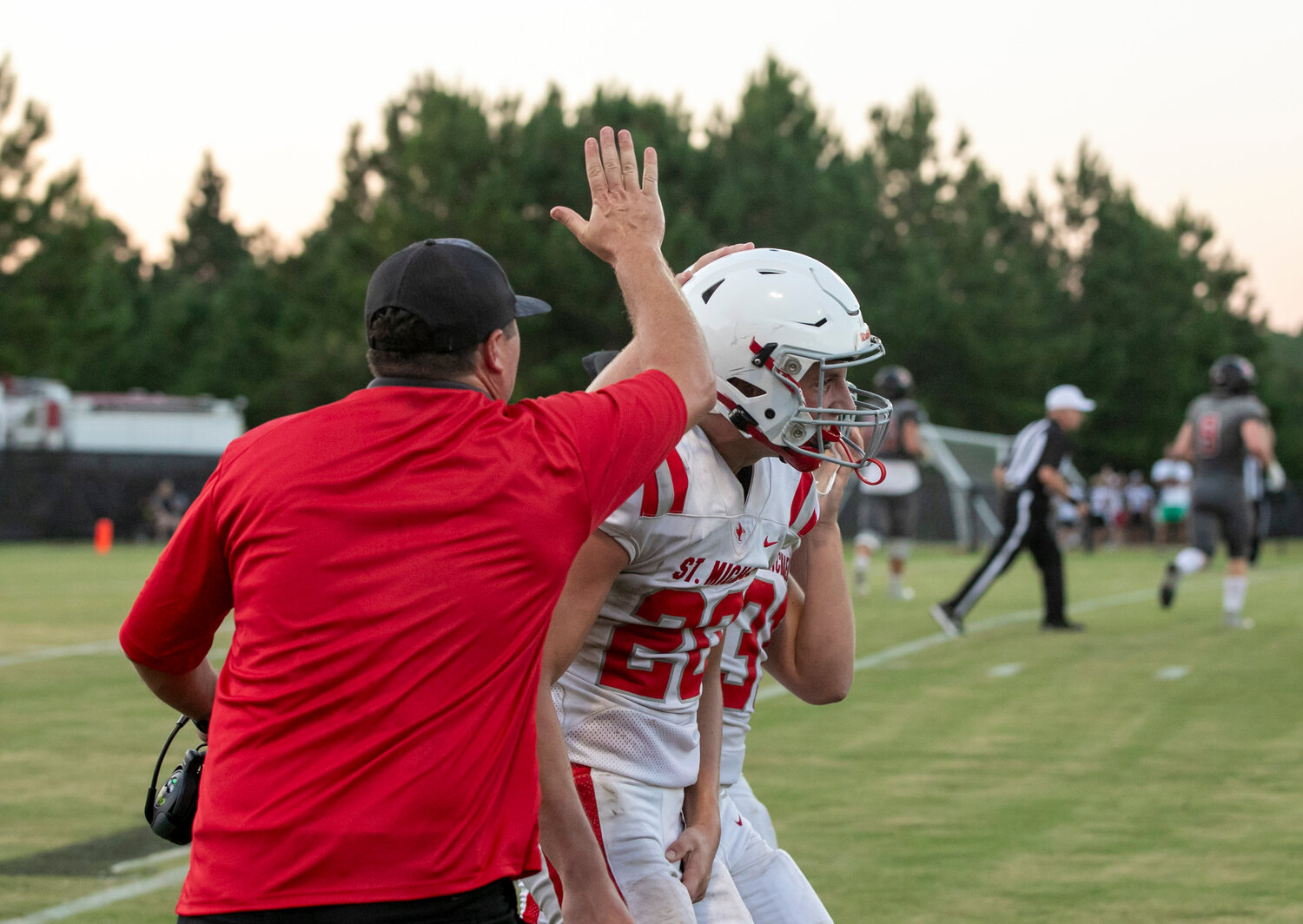 Gus Faulkner (20) returns to the St. Michael sidelines after an interception and is greeted by Cardinal defensive coordinator Simon Cortopassi Thursday, Aug. 17, during the preseason jamboree against the Spanish Fort Toros.