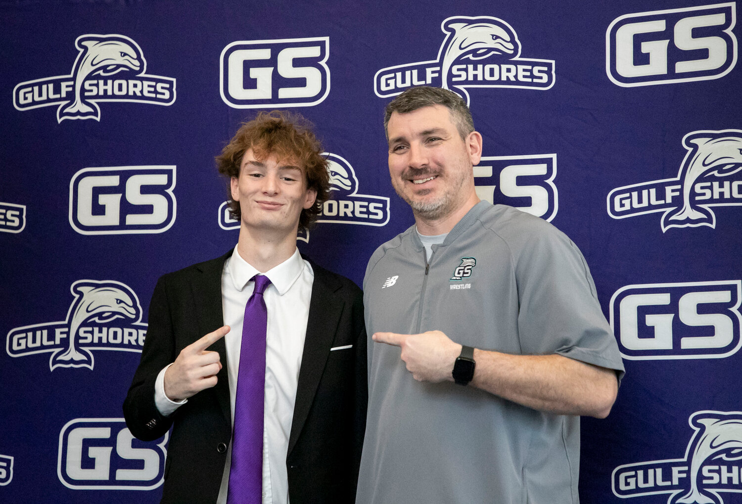 Dolphin senior Ethan Sharkey poses with Gulf Shores head wrestling coach Britt Shaw during Wednesday’s signing ceremony at the high school. Shaw said he was triple-happy as Sharkey’s wrestling coach, former cross country coach and friend of the family.
