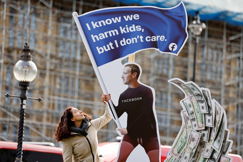 A demonstrator poses with an installation depicting Facebook founder Mark Zuckerberg surfing on a wave of cash and surrounded by distressed teenagers, during a protest opposite the Houses of Parliament in central London on Monday, Oct. 25, 2021, as Facebook whistleblower Frances Haugen is set to testify to British lawmakers. (Tolga Akmen/AFP/Getty Images/TNS)