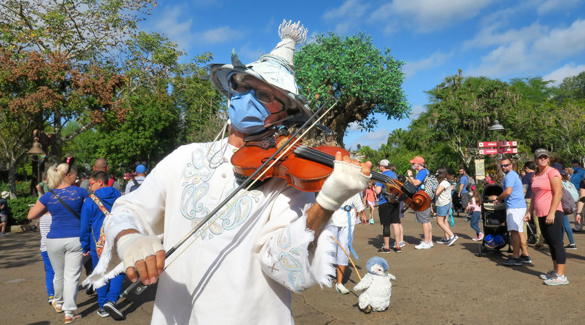 A street performer, masked for COVID protocol, plays violin as a part of the Merry Menagerie troupe at Disney's Animal Kingdom, Thursday, Dec. 30, 2021. Walt Disney World's four Florida theme parks filled to near-capacity for the New Year's Eve holiday, in Lake Buena Vista, Florida. As of Thursday afternoon, Animal Kingdom was the only park showing available reservations for ticket holders, Disney resort guests and annual passholders for New Year's Eve, Jan. 31. (Joe Burbank/Orlando Sentinel/TNS)
