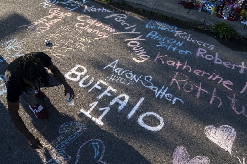 Aaron Jordan, of Buffalo, adds to a sidewalk chalk mural depicting the names of the people killed  as people gather at the scene of a mass shooting at Tops Friendly Market at Jefferson Avenue and Riley Street on Sunday, May 15, 2022, in Buffalo, NY.  (Kent Nishimura/Los Angeles Times/TNS)