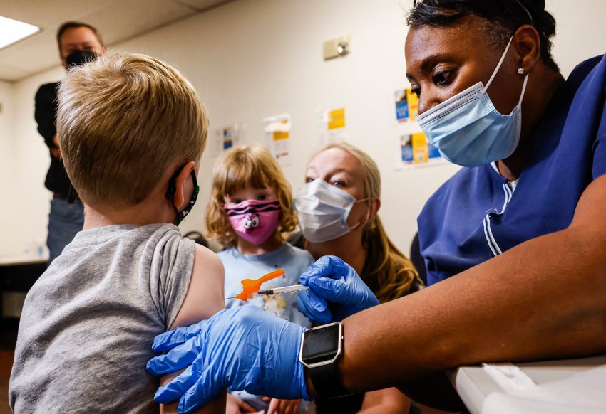 Registered nurse Barbara Davis, right, administers a Pfizer COVID-19 vaccine on Robert Holt, 5, left, as his mother Jennifer, middle right and her sister Elizabeth, 3, watches on Tuesday, May 24, 2022 in Dallas.