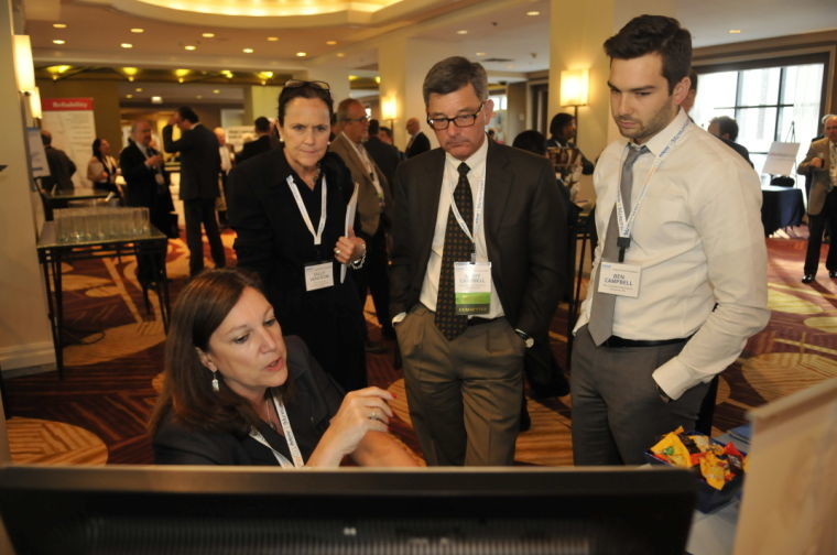 Deb Dreyfuss-Tuchman of AdPay demonstrates a product for Sally Hendron of The Daily Journal, and Scott and Ben Campbell of The Columbian Publishing Monday at the Inland Press Association 128th Annual Meeting at Renaissance Chicago Hotel.