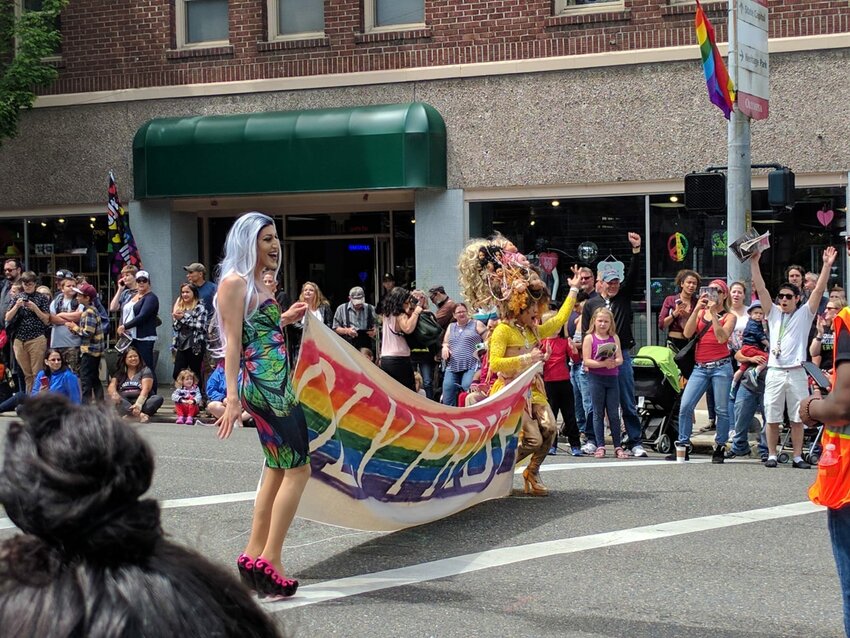 Oly Pride banner held by two drag queens while onlookers enjoy the Olympia Pride Parade, 2017.
