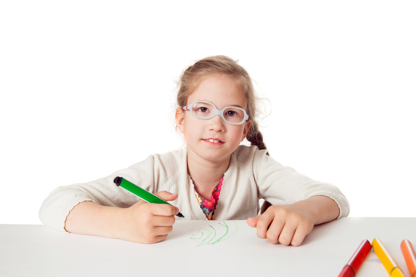 The little girl with glasses is drawing on a white surface.