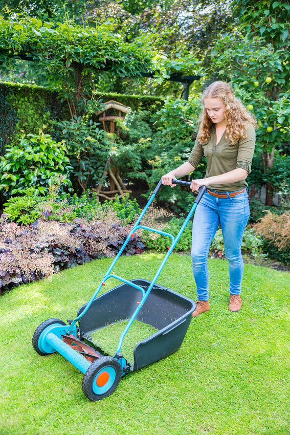Young woman pushing a lawn mower on grass
