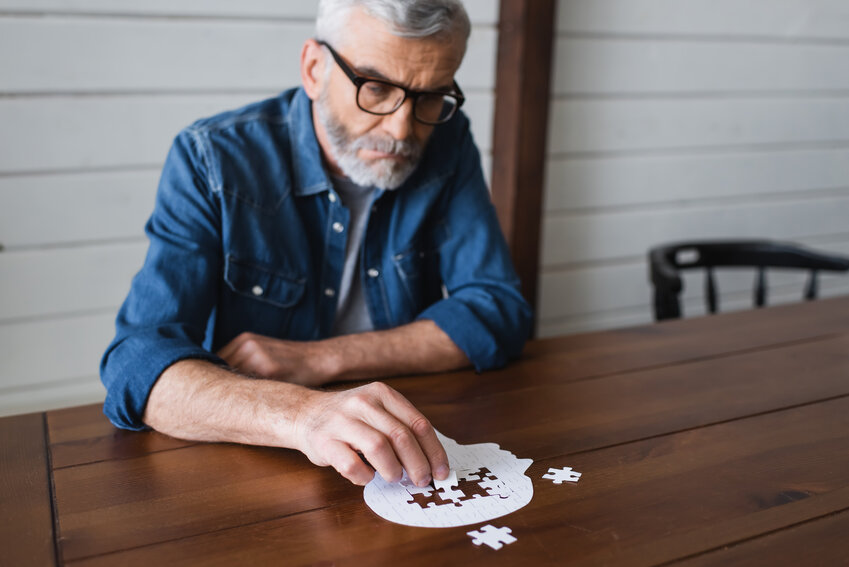 A man puts a puzzle piece into a head-shaped puzzle on a table. Memory and dementia concept.