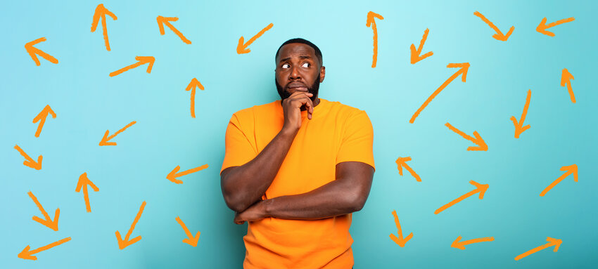 Conundrum of decisions concept photo. A black man in an orange shirt is pensive and worried with many arrows going in many directions.