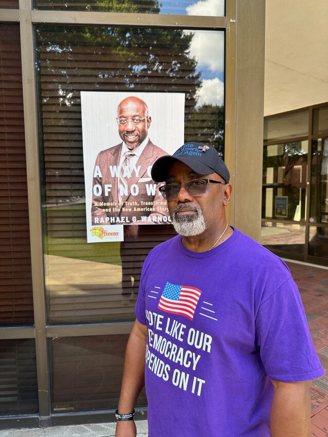 Jarvis is standing in front of a photo of the cover of Reverend Senator Raphael Warnock's book.