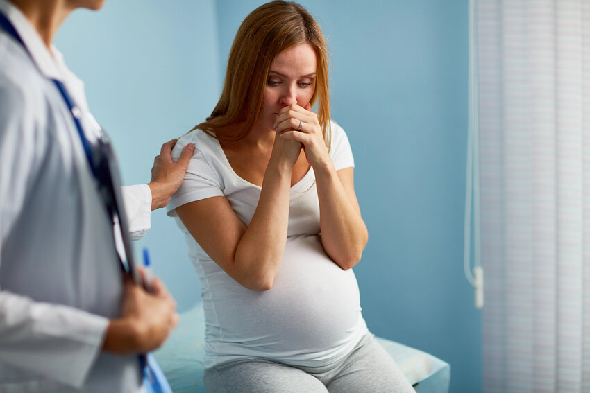 A pregnant woman looks worried while at a doctor's appointment.