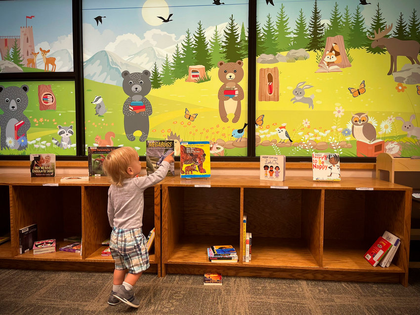 Logan Whorley, age 1, engages with the book display in front of the newly painted &quot;window&quot; mural at the Lacey Timberland Library.