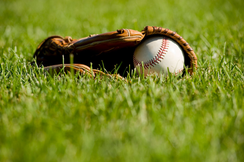 A white baseball in a brown leather baseball glove lying on a green baseball field.