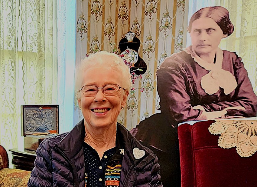 Docent Cheryl Hougham with Susan B. Anthony looking over her shoulder. Susan leans on the chair she was reputed to have sat in during her 1871 visit, 2023.