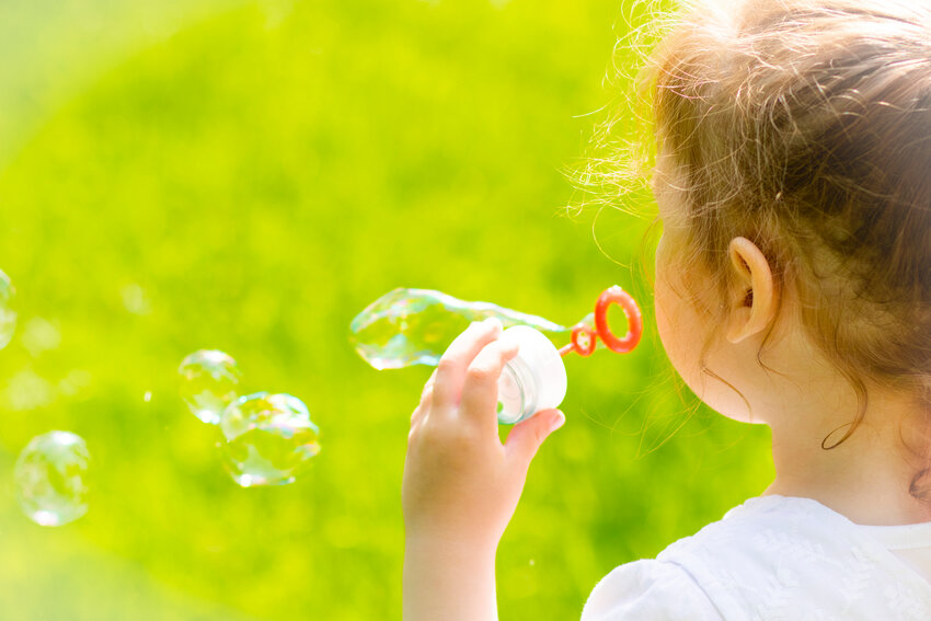 A little girl blows bubbles outside.