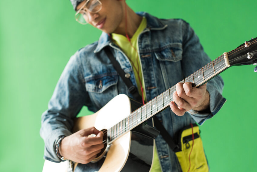 Image of a man playing a guitar with a happy soft expression on his face.