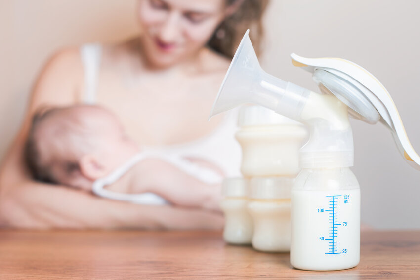 Manual breast pump with a mother feeding her baby in the background, mothers breast feeding their babies contributes to the good health of both babies and mothers.