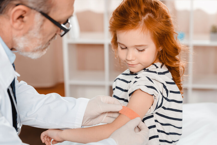 A doctor puts a bandaid on a small girl's arm after a vaccination.