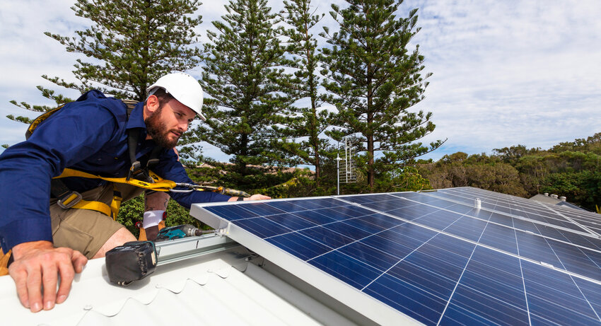 Solar panel technician with drill installing solar panels on roof