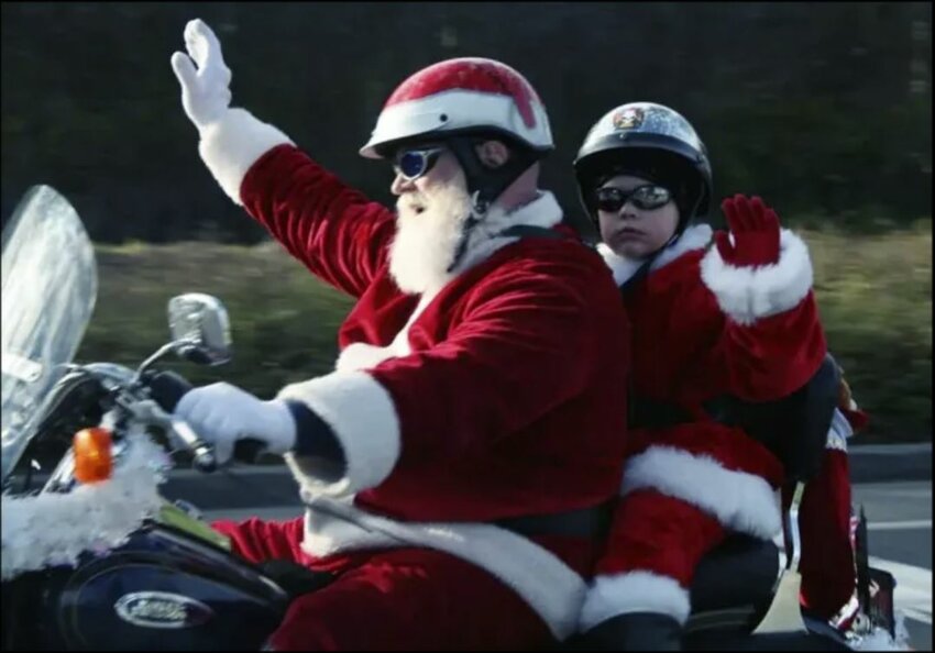 Santa on a motorcycle with a child waving while riding during a previous Olympia Toy Run