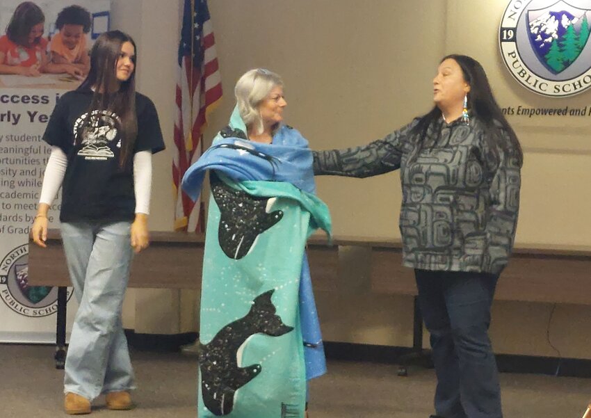 Outgoing Superintendent of North Thurston Public Schools Dr. Debra Clemens (center) is honored with a Coast Salish Indian blanketing ceremony. River Ridge student Francheska Helton (left) and Native Student Program paraeducator Laura Bowman (right) bestow the blanket. The event happened as part of the NTPS School Board and Nisqually Tribal Council joint meeting.
