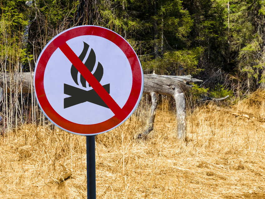 A fire burning ban sign in front of dry grass and trees.