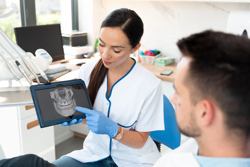 A woman dentist shows a male patient a digital rendering of a jaw and teeh