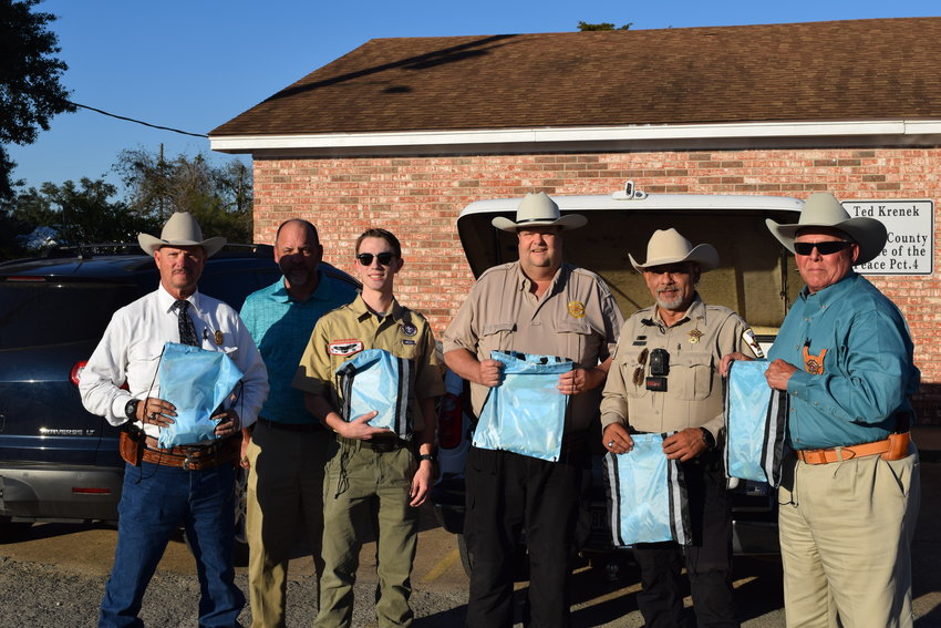 Seth Reid (third from left) poses with his father (blue polo shirt), Waller County Precinct 4 Constable Joel Trimm (center), deputy constables and officers from the Waller County Sheriff&rsquo;s Office. The bags being held up are care packages for young children that may need comforting when dealing with stressful situations law enforcement becomes involved in. Reid created the care packages as part of his work toward becoming an Eagle Scout.