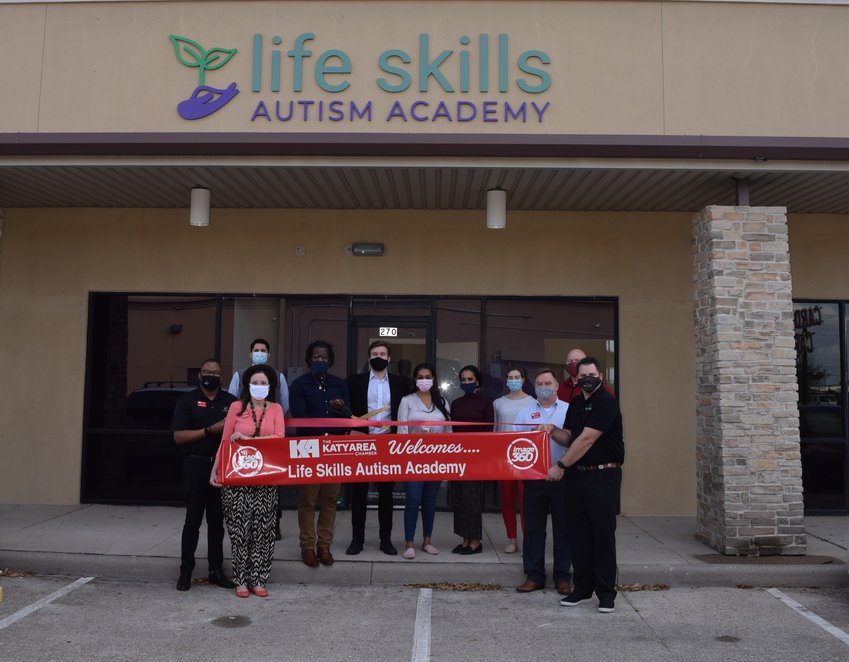 Dehazard Allen (center with scissors), clinical director of Life Skills Autism Academy in Katy is joined by Life Skills Autism Academy program director Nathan Rabens (behind scissors) and members of the Katy Area Chamber of Commerce and other academy staff for the autism clinic&rsquo;s March 9 ribbon cutting.