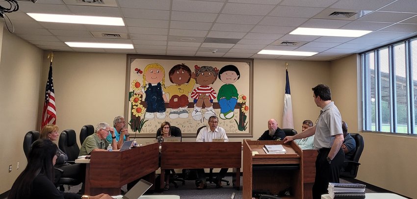 Chris Brown (at podium) addresses Pattison City Council during Tuesday evening&rsquo;s meeting &ndash; the first in-person meeting for the city&rsquo;s governing body since the pandemic forced them to go remote. Council met at the Royal ISD Administration Building, but may soon have their own council chambers to hold meetings in. Pictured from left to right: Deputy City Secretary Andrea Govea, City Secretary Lorene Hartfiel, Council Member Robert MacCallum, Council Member Wayne Kircher, City Attorney Lora Lenzsch, Mayor Joe Garcia, Council Member Seth Stokes, Council Member Frank Cobio, Jr. and Council Member Fred Branch (behind Brown).