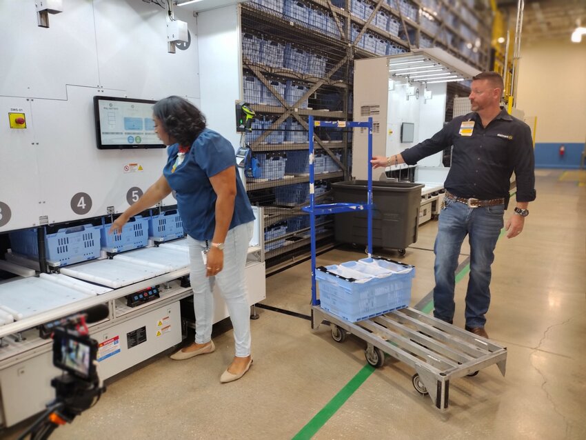 Walmart team lead Anna Mearidy (left) and store manager Robert Smith demonstrate how a customer order is fulfilled after robots bring the requested items to the Static Work Station at Walmart&rsquo;s fulfillment center at 25108 Market Place Drive in Katy.