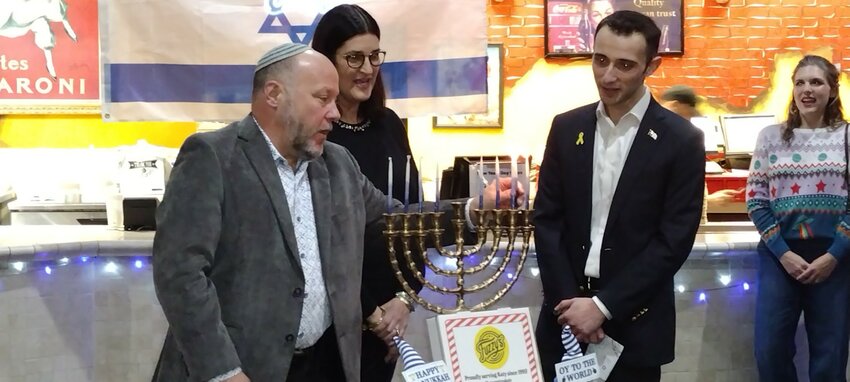 Rabbi Scott Hausman Weiss (left) lights all the candles on the menorah in celebration of the eighth night of Hanukkah on January 1 at Fuzzy&rsquo;s Pizza, 613 S. Mason in Katy, as Elyse Spector Kalmans (center), board chair of the Holocaust Museum Houston looks on. Fuzzy&rsquo;s owner, Jeff Hajjar (right) said that 18 percent of the evening&rsquo;s proceeds would be donated to the museum. International Holocaust Remembrance Day is January 27, said Kalmans.